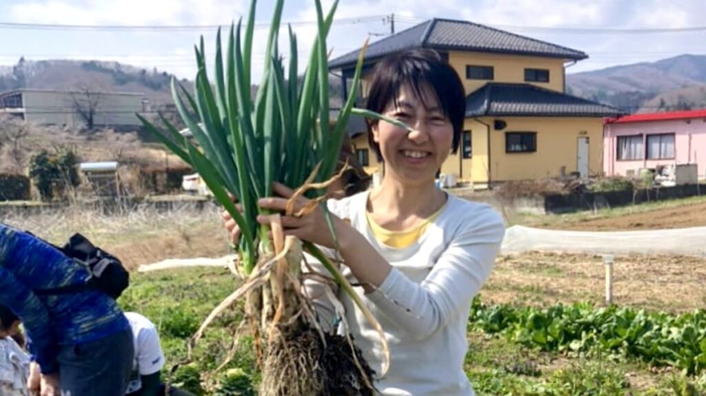 ときがわ町の畑ヨガ＆お野菜収穫で採れたネギを持つ東松山ヨガの主宰の原田政子